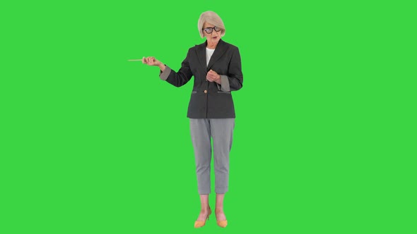 Confident Senior Lady Teacher Explaining and Pointing at Something on a Green Screen, Chroma Key.