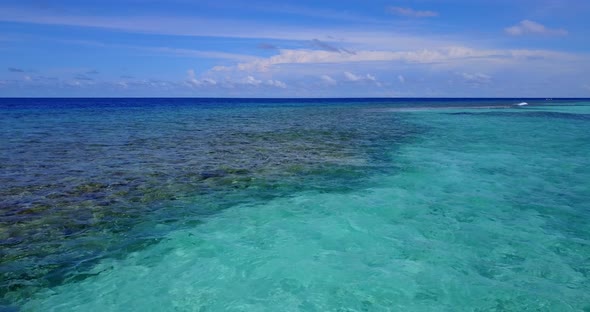 Daytime flying tourism shot of a sandy white paradise beach and aqua blue water background in high r