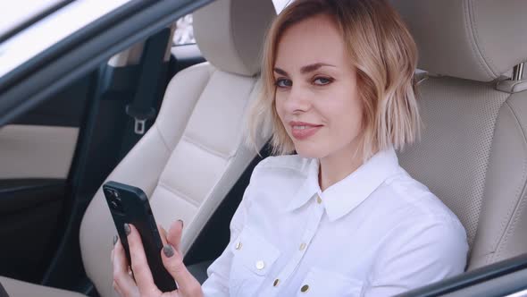 Beautiful Young Woman Sitting in a Car on Drivers Seat and Using Smartphone