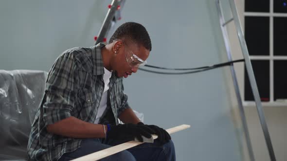 Young Black Worker with Goggles Polishes Wooden Plank