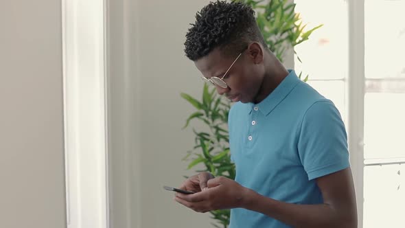 Thoughtful African American Student in Eyeglasses Using Smartphone.