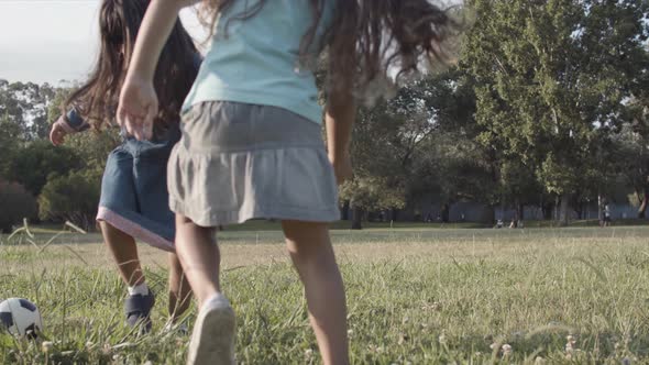 Two Long-haired Latin Girls Kicking Ball on Meadow