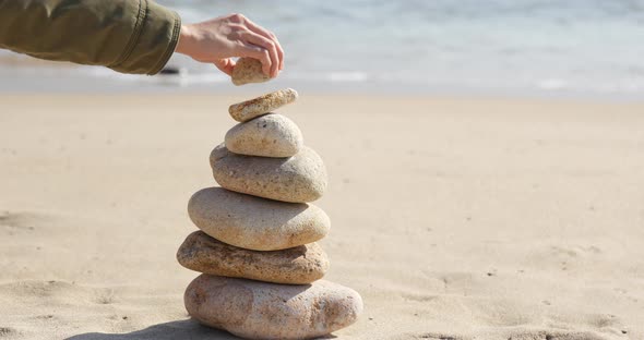 Woman hand put pebble in pyramid on the sea 