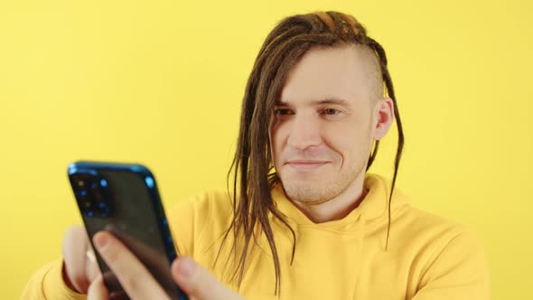 Young Happy Man Browsing Mobile Phone on Yellow Background