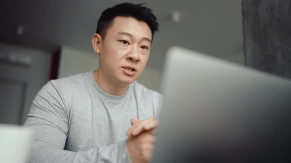 Asian concentrated man talking by video call on laptop