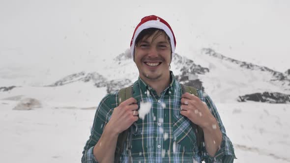 A Snowball Flies Into the Face of a Funny Guy in a Christmas Hat on the Background of Mountains