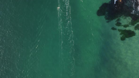 A fishing boat dragging nets around a rugged coastal headlands to catch schools of fish. High drone