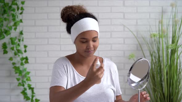 Young woman with eyes closed spraying facial mist at home