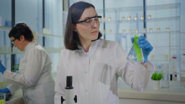 a Positive Female Scientist in a White Coat in a Modern Laboratory Smiles and Looks Through a