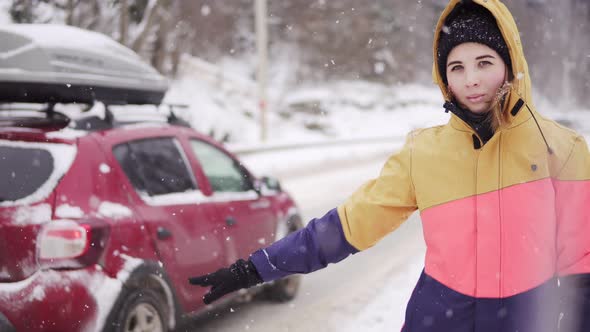 Woman in Bright Winter Clothes Hitchhiking in Winter at the Road