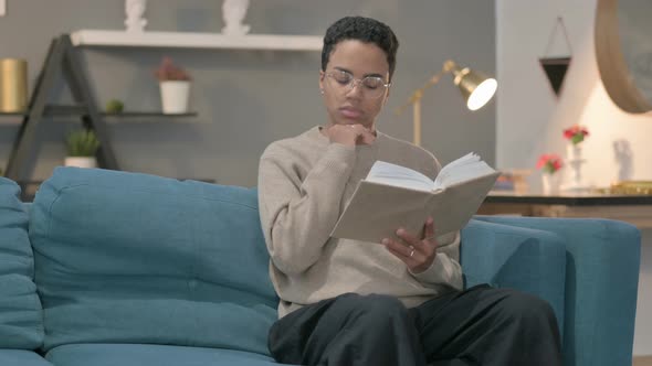 African Woman Thinking While Reading Book in Sofa