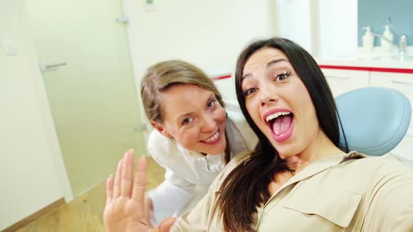 Close up of happy female patient with dentist looking at camera and waving