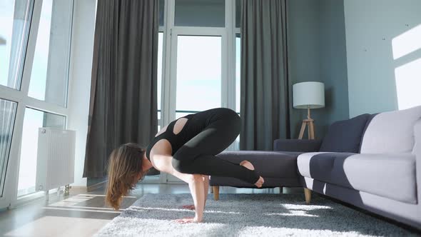 Young Caucasian Woman in Black Jumpsuit Doing Handstand Bakasana at Home to Develop Power