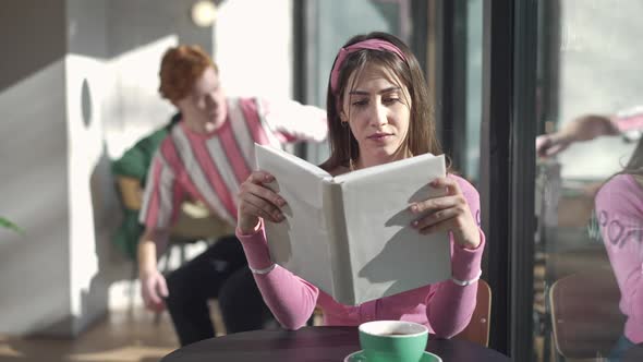 Portrait of Absorbed Intelligent Retro Woman Reading Book in Coffee Shop in 1980s