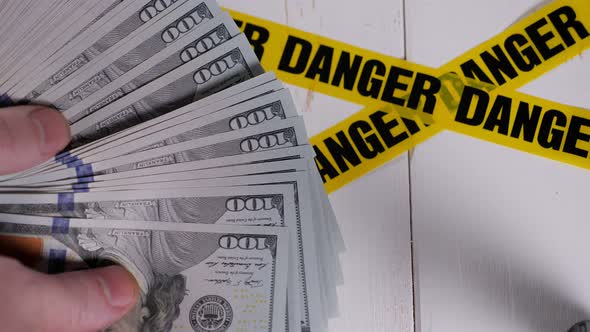 A Man Putting a Stack of Hundred Dollar Bills on a Yellow Warning Tapes DANGER