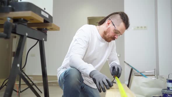 Carpenter in Protective Gloves and Glasses Makes Measurements on Wood