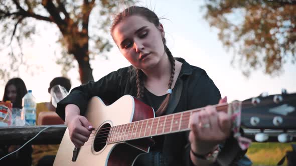 A Young Girl in Nature Plays the Guitar During a Picnic with Friends