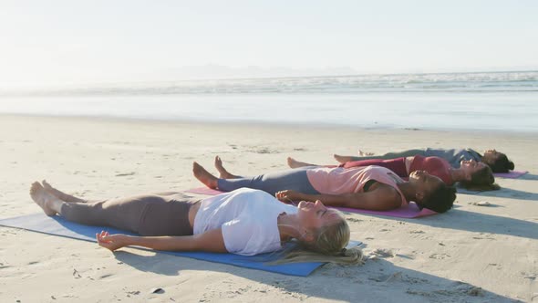 Group of diverse female friends practicing yoga, lying on mats at the beach