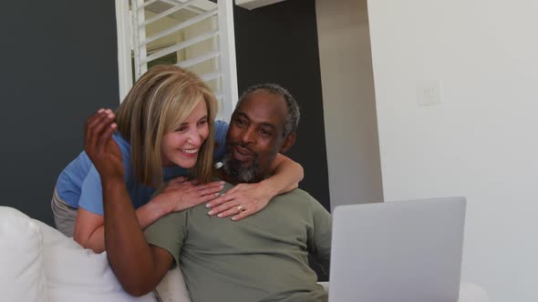 Mixed race senior couple using laptop while sitting on the couch at home