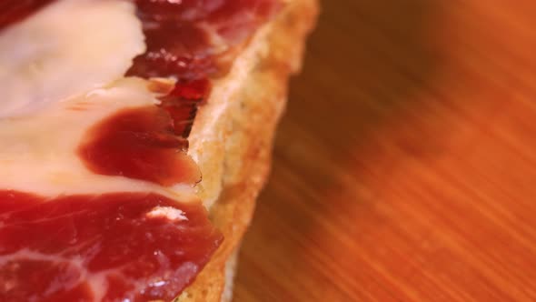 Very fatty cured ham slice on top of bread, macro shot. Rotating motion of traditional spanish pinch
