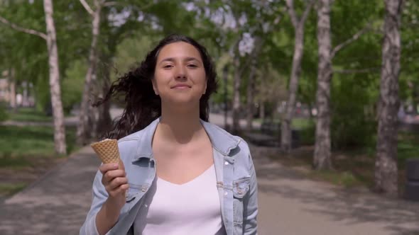 A Beautiful Young Girl Walks Down the Street and Eats Ice Cream on a Hot Summer Day