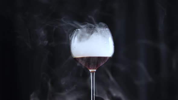 Glass Filled with a Dark Drink and Smoke with a Black Background