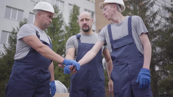 Three Young Caucasian Workers Putting Hands on Each Other, Shaking Heads and Starting Work