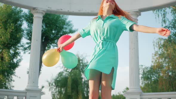 Beauty girl with red hair and colorful air balloons spinning and laughing, on white background. Beau