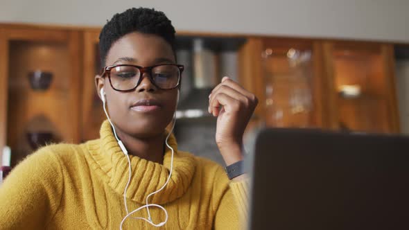 African american woman wearing earphones using laptop while working from home