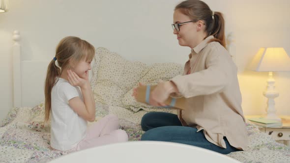 Young Woman Is Giving Present To Happy Girl and Clapping Hands Making Surprise To Child