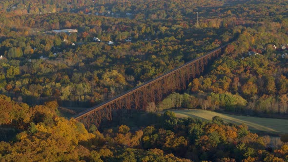 Aerial of railroad bridge between valley covered with autumn forest