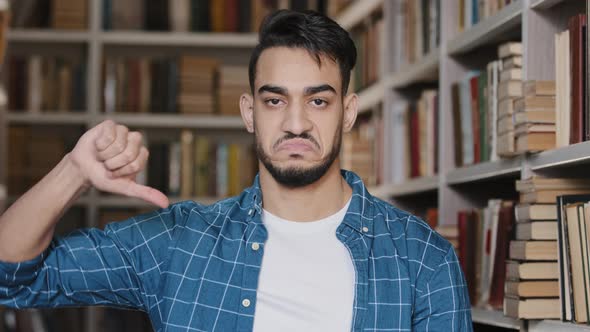 Closeup Dissatisfied Upset Indian Man Student Looking at Camera Standing in Library Showing Thumb