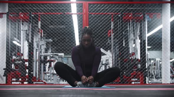 An Africanamerican Woman Sitting on Yoga Mat in the Gym and Leaning Forwards