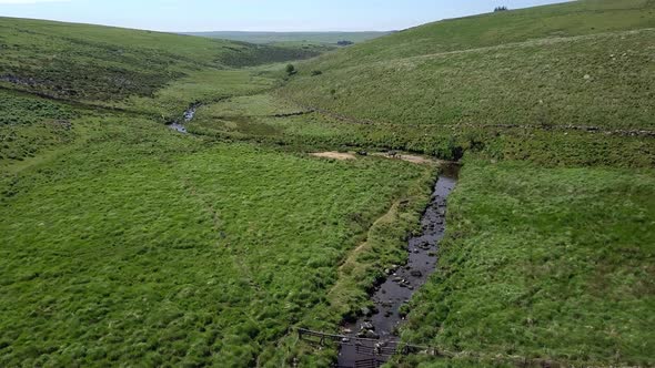 Very slow forward tracking aerial shot over a Dartmoor creek river with a perpendicular bend. Devon,