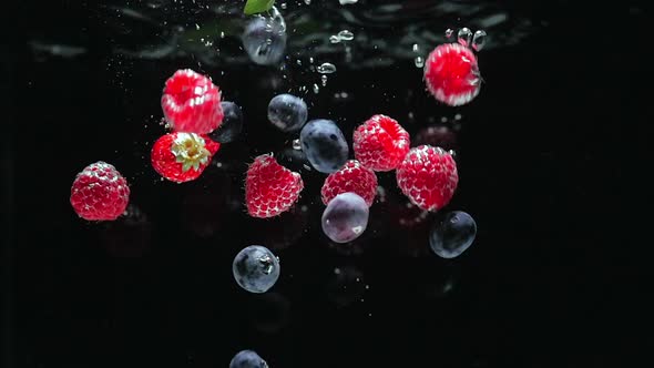 Fresh Raspberries with Blueberries and Fresh Mint Leaves Fall on a Black Background Into the Water