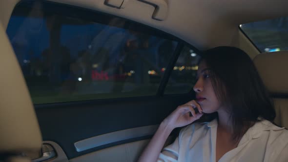 young Asia businesswoman looking out of window car while sit on passenger back seat in urban city.