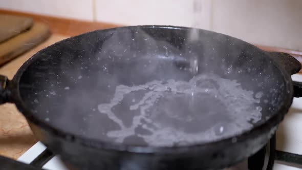 Pouring Water From Glass in Hot Greasy Skillet