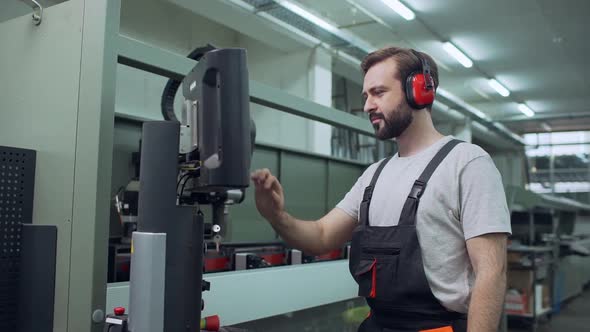 Portrait of Adult Employee Man 30s Wearing Working Overall and Headphones Touching with Equipment