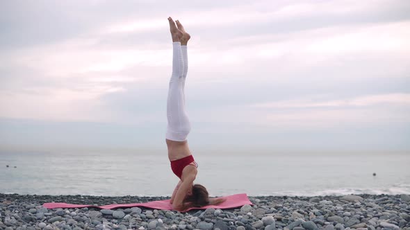 Woman Doing Headstand on Beach on Yoga Mat.