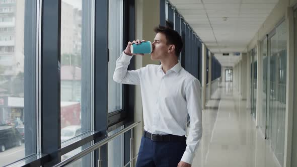 Thoughtful Businessman Looks Out the Window in Office and Drinks a Cup of Coffee