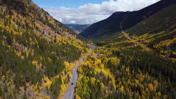 Descending next to Colorado highway surrounded by golden aspens in the fall, Aerial