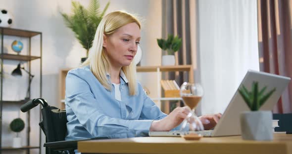 Businesswoman Sitting in Wheelchair After Accident and Working on Computer at Home in Daytime