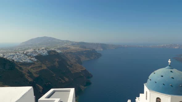 Pan up view over iconic caldera and blue rooftop church Santorini Greece