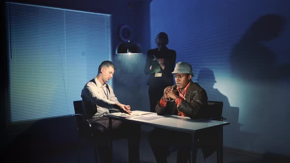 Black Prisoner in Handcuffs Having Interview with Caucasian Detective in Interrogation Room