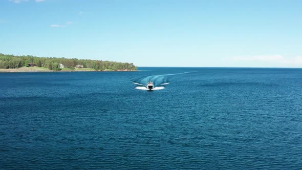 Aerial, luxury speedboat sailing fast on vast blue ocean next to island.