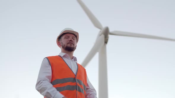 The Engineer, a Man in an Orange Vest and White Hard Hat, Folds His Arms and Stares Confidently at