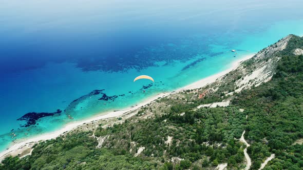 Drone view of paragliding over scenic hill and coastline.