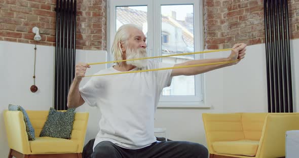 Man in Sportswear Sitting on Fitness Ball and Stretching with Elastic Tape During Training at Home