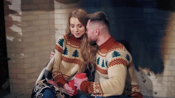 Beautiful loving couple resting near fireplace. Young woman and a man with cups of drink 