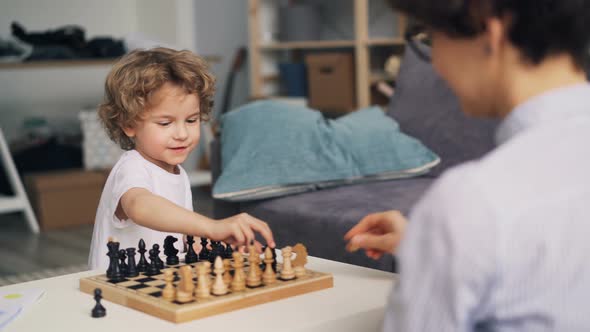 Joyful Boy Having Fun with Chess Pieces While Mom Teaching Him To Play Game